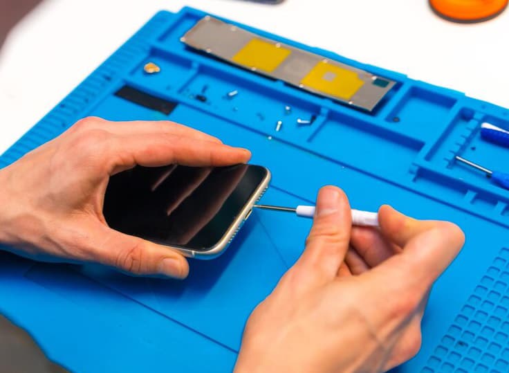 A technician repairing an Android smartphone on a workbench with precision tools and spare parts laid out